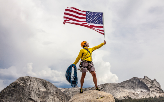 Climber waves an American Flag from the summit after a challenging ascent.