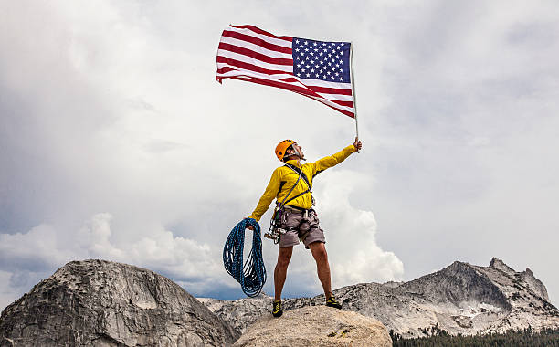 Climber raising an american flag on the summit. stock photo