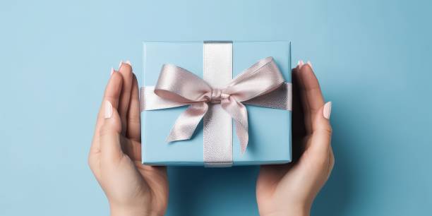 istock Female hands with festive minimalistic manicure tie a bow on blue gift box 1493376461
