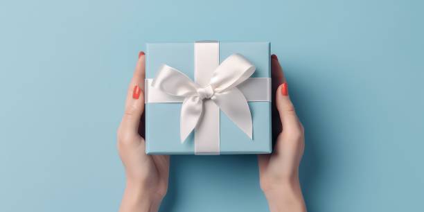 istock Female hands with festive minimalistic manicure tie a bow on blue gift box 1493376476