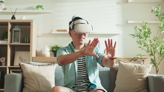 Asian exited male man wear VR or virtual reality glasses,headsets sit relax playing explore new world online at living room in front of TV at home in quarantine period technology and innovation ,A Man excited in virtual reality