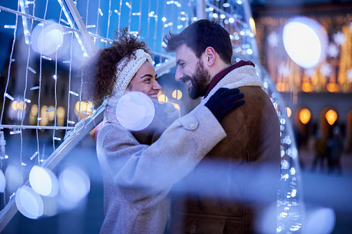 Young happy couple communicating while spending a night inside of Christmas lights in the city.