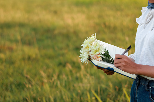 woman writing in a book with a bunch of beautiful flowers. woman in hijab writing while standing outdoors