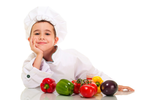 Little happy boy chef in uniform with vegatables lean on hand isolated on white