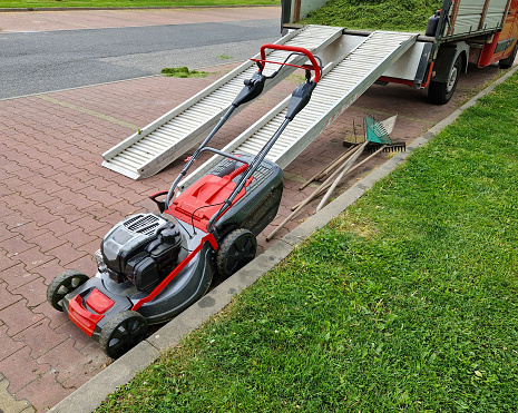 a truck loaded with cut grass. ramps for large mowers made of aluminum profiles. a lawnmower is waiting ready to work in the parking lot of a shopping center. red, cultivation, lawnmower, mowed, outdoor, mower,