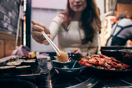 An Asian woman is enjoying the local Korean cuisine in the Tsuruhashi area of Osaka, Japan. Tsuruhashi is the largest Korean community in Japan, making Korean food a must-try culinary experience in the area.