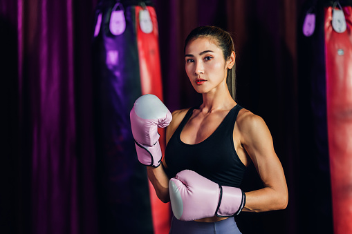 Female Boxer training in Boxing Club. Woman Boxing fighters training at gym. Strong muscular woman practicing box in pink boxing gloves in gym.