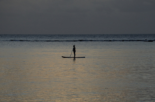 Albion, Mauritius - April 23, 2023: Silhouette of a person, who enjoys Stand Up Paddling at the beach of the Indian Ocean in Mauritius during sunset.