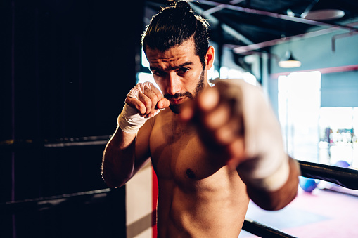 Handsome young Caucasian male kickboxer punching a boxing bag at the gym. He is focused and determined. He is strong and fit.