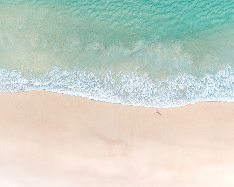 Aerial view of man standing at coastline. Sea, waves, algae and sand.Beach detail