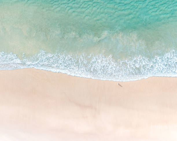 Beautiful beachside destinations pictured with sand, pristine blue water and gentle waves breaking on a beach Beautiful beachside destinations pictured with sand, pristine blue water and gentle waves breaking on a beach spume stock pictures, royalty-free photos & images