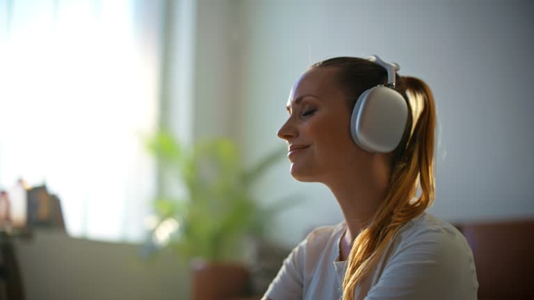 SLOW MOTION Beautiful,serene young woman with blonde ponytail putting on headphones,meditating in living room at home. Healthy lifestyle,wellbeing,mindfulness,tranquility,domestic life,lifestyle. Shot in 8K Resolution.