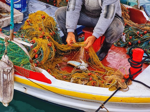 A male fisherman in the boat holding a fishing net and collecting the catch of the day