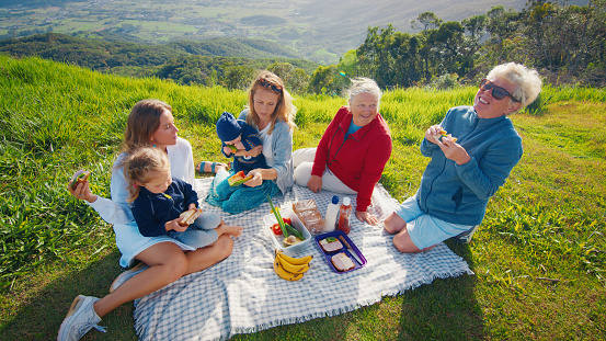Big family have picnic on the green hill in the mountains at sunrise