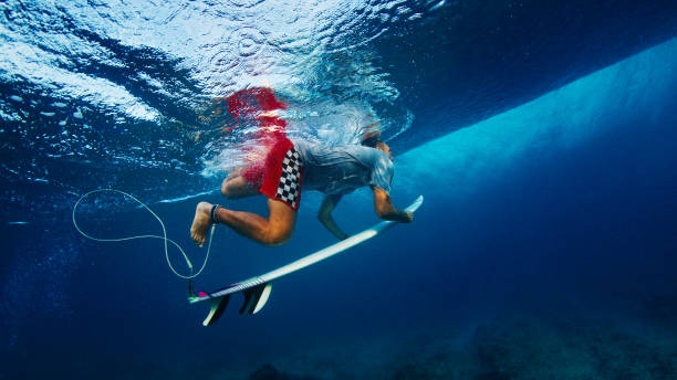 surfer pod falą. męski surfer nurkuje pod falą z deską surfingową w krystalicznie czystej tropikalnej wodzie - przeniesienie na dół zdjęcia i obrazy z banku zdjęć