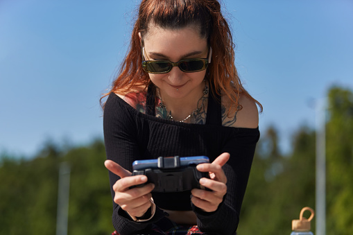 Happy diverse female with chest tattoo plays online video game on a smart phone with attached joystick