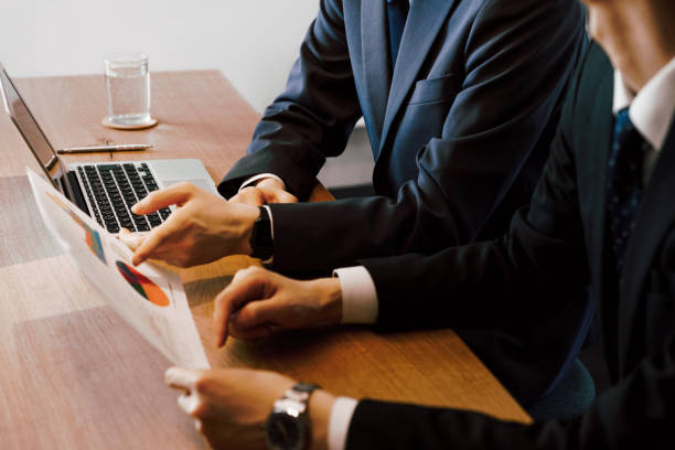 オフィスのミーティングテーブルで資料を並べて見ながら相談するスーツ男性2人 - ビジネス ストックフォトと画像