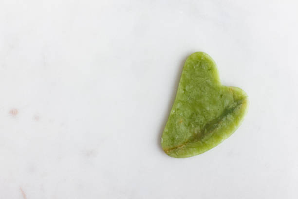 istock Green jade gua sha massager for face on white marble. 1493420973