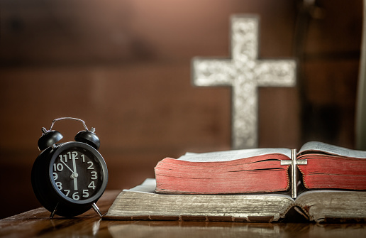 Alarm clock with the cross and holy Bible on wooden table in the morning. christian concept.