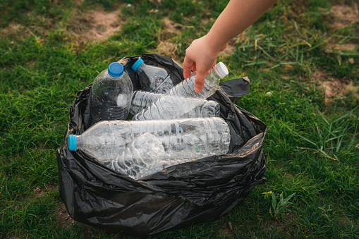 Close up hand collects garbage plastic in a park. A volunteer cleaning plastic bottle on a grass. Environment, recycle and protection concept.