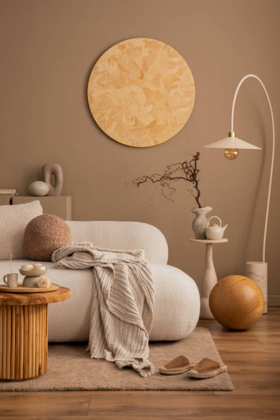 istock Creative composition of living room interior with round wall panel, beige sofa, stylish lamp, wooden coffee table, brown pillow, slippers, brown rug and personal accessories. Home decor. Template. 1493432249