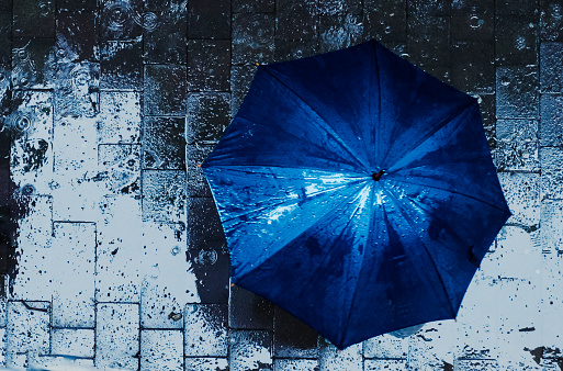 A blue umbrella photographed from a high angle, on a rainy evening, with beautiful reflections on the pavement  and a nice contrast between light and dark