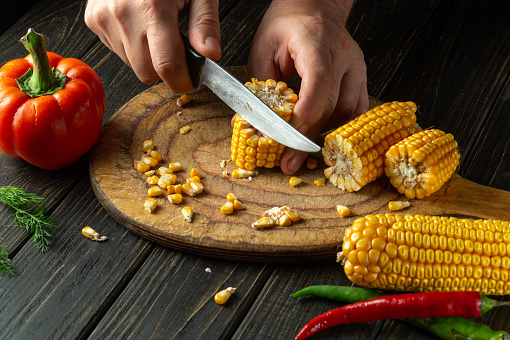 The cook cuts corn with a knife. Maize is a great diet breakfast or lunch. Working environment at the kitchen table.