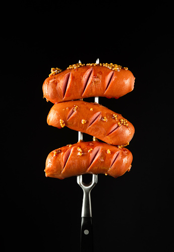 Grilled with mustard three sausages on a fork. Delicious street food concept on black background. Copy space