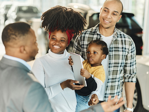 Happy African American family communicating with male salesperson in a car showroom.