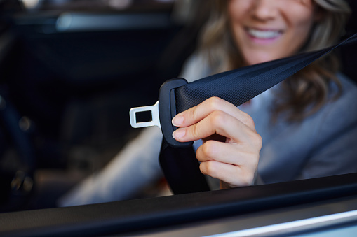 Close up of unrecognizable woman fastening seatbelt before a trip by car.