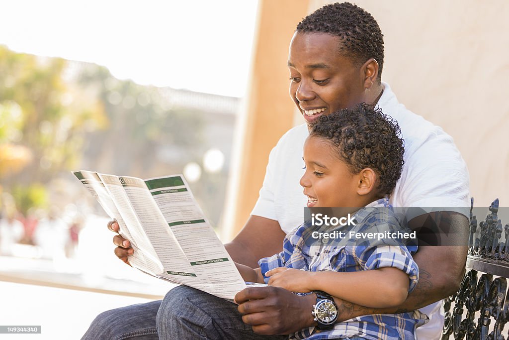 Mixed Race pai e filho, lendo Park folheto do lado de fora - Foto de stock de Folheto - Publicação royalty-free