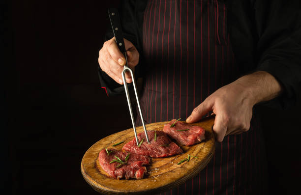 istock The cook holds a fork in his hand and a cutting board with beef steaks before barbecue. Black space for restaurant recipe or hotel menu. 1493444769