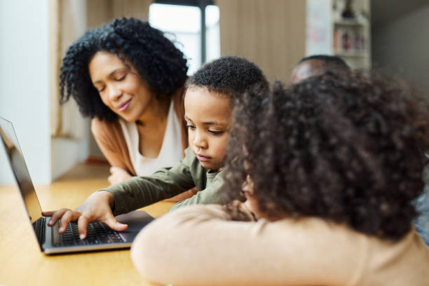 istock Small black boy using laptop with his mother and sister at home. 1493445019