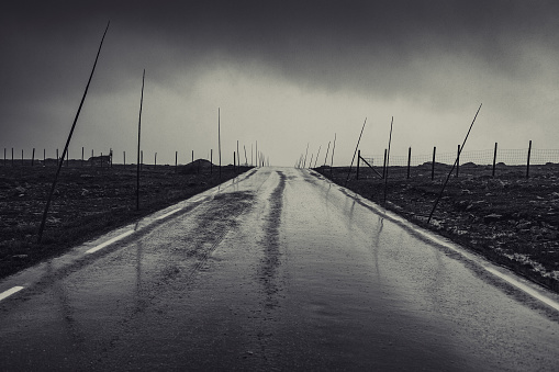 Dramatic road in Norway at rain. Dark black and white film style colors.