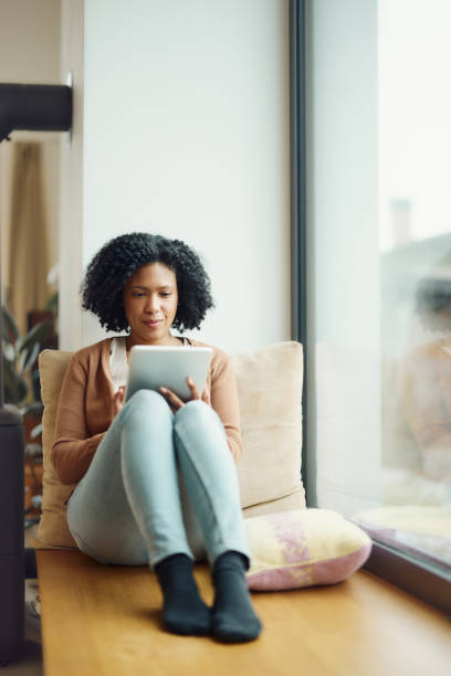 istock Smiling black woman using touchpad by the window at home. 1493445485