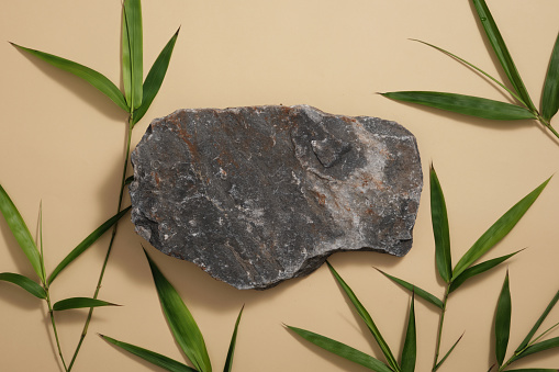 Gray stone and green bamboo leaves are decorated on brown background. Minimal scene with blank space for display cosmetic product. Top view, flat lay.