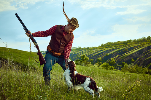 Portrait of hunter with rifle and hunting dog while chasing the prey in the field.