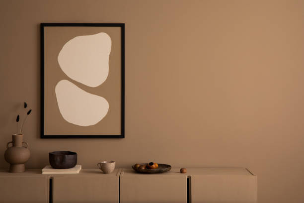 istock Creative composition of warm living room interior with mock up poster frame, copy space, brown sideboard, book, vase with dried flowers and personal accessories. Home decor. Template. 1493447056