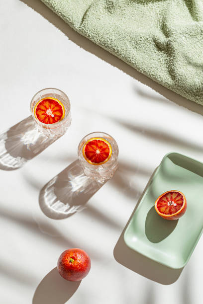 istock Creative composition made of two glasses with cocktail, half bloody red orange on a tray on white background with palm tree leaf shadow. Summer refreshment and party concept. Minimal style. 1493449092