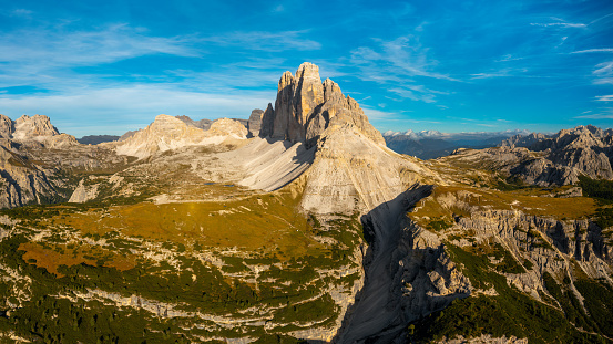 High Stone Columns and Battlement-Like Peaks of Tre Cime di Lavaredo's Mountain Massif, Enveloped in the Golden Hues of Sunset, Underneath a Breathtaking Blue Sky with White Clouds.