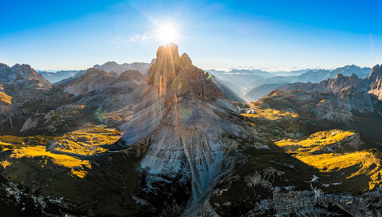 Mountain landscape of Three Peaks of Lavaredo at sunrise. Sunny jagged peaks and broad hilly shaded highlands covered with grass and sand aerial view