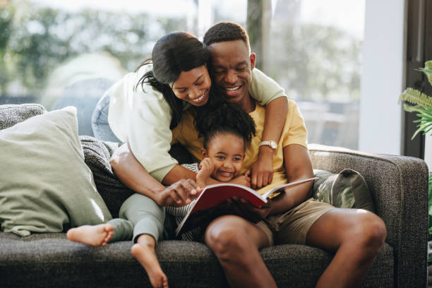 des parents lisent un livre avec leur fille. famille noire heureuse à la maison - family reading african descent book photos et images de collection
