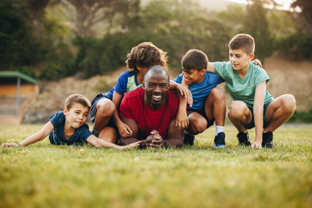 school coach and his team lying in a sports field - soccer child coach childhood imagens e fotografias de stock