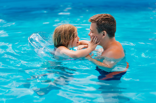Dad and daughter have fun and swim with inflatable circle in the pool. Dad teaches his daughter to swim. family holidays and sports with children. Happy family. Father's Day.