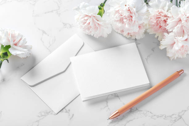 istock White blank card and envelop with pen and pink flower on marble background 1493461303