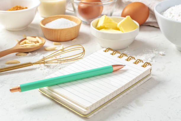 istock Notepad and pen for recipe with baking or cake ingredients in bowls, butter, nuts, eggs, sugar on marble table 1493461324