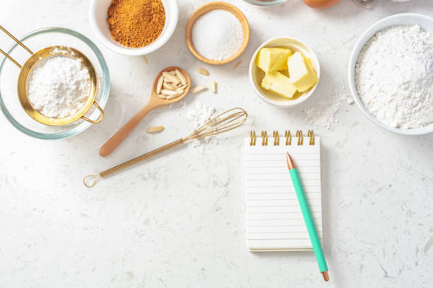 istock Notepad and pen with baking ingredients in bowls, flour, nuts, eggs, sugar and gold sieve and whisk 1493461418