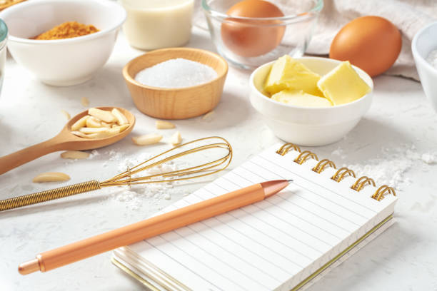 istock Notepad and pen with baking ingredients in bowls and gold whisk on marble table 1493461477