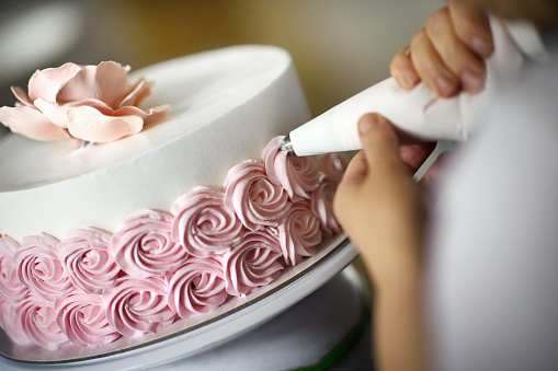 Closeup of an unrecognizable woman putting icing on a strawberry cake at a small family owned cake shop.