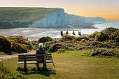 Senior man sitting on bench looking at view of Seven Sisters cliffs on south coast of England